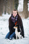 Frau sitzt mit Sheltie im Schnee