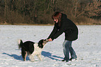 junge Frau spielt mit Hund im Schnee