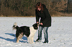 junge Frau spielt mit Hund im Schnee